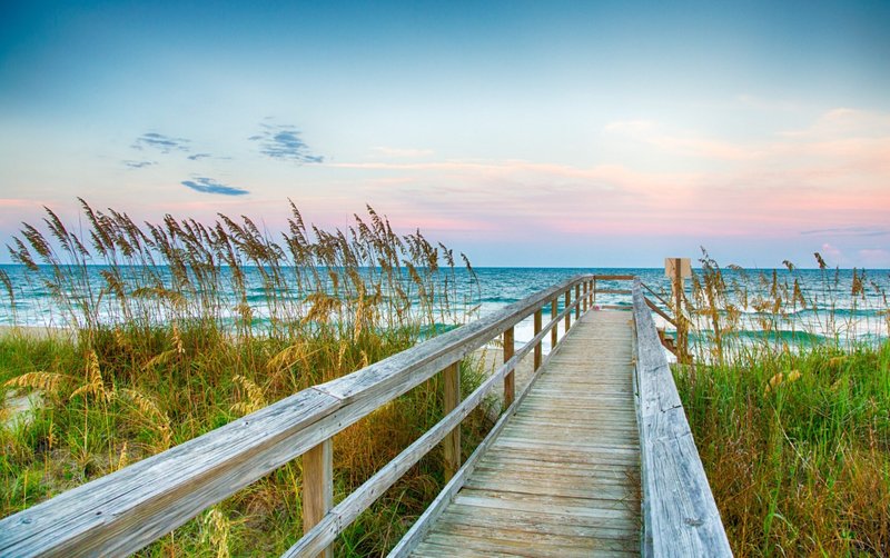 A wooden beach access boardwalk leading through sea oats to the ocean near Jacksonville, NC.