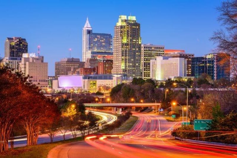 Downtown Raleigh, North Carolina skyline at dusk with highway light trails and illuminated buildings.