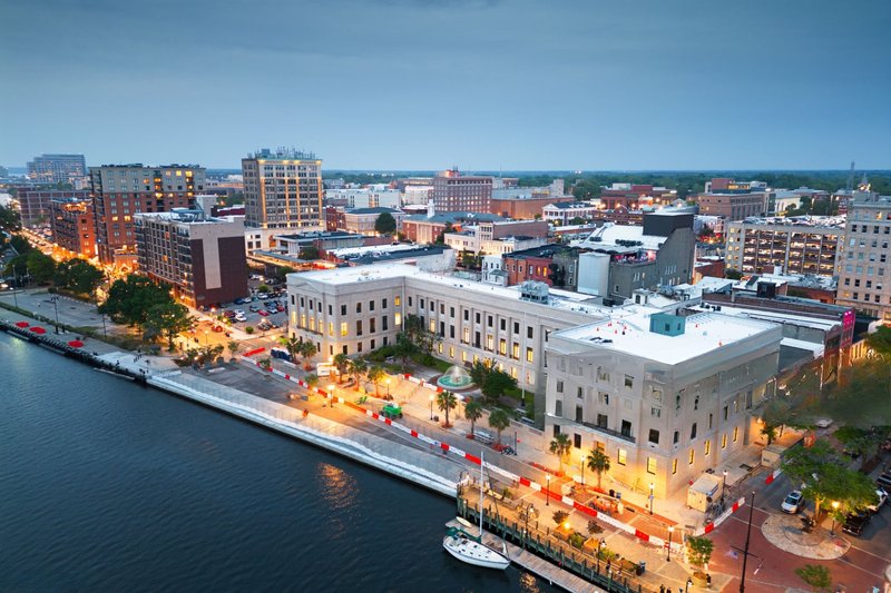 Aerial view of downtown Wilmington waterfront at dusk with city lights along the river in Wilmington, NC.