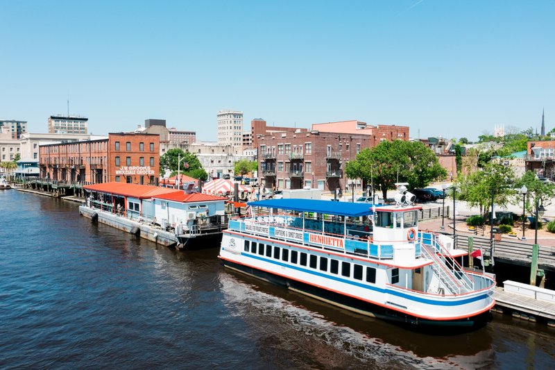 Riverboat docked along the Wilmington Riverwalk with historic buildings nearby in Wilmington, NC.